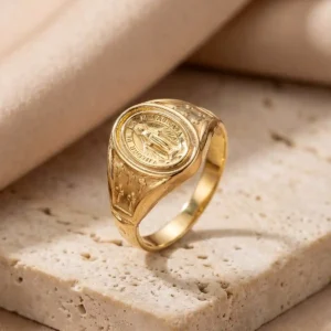 Anillo de la Virgen de la Milagrosa en tono oro sobre base de piedra beige con estilo premium en Luxor SM Joyería Santa Marta.