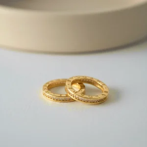 Anillos Bulgari en tono oro con circones exhibidos en superficie clara en Luxor SM Joyería Santa Marta.