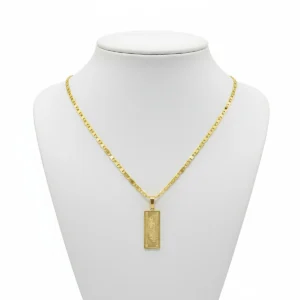 Cadena escalera plana con dije tipo billete de 100 dólares en oro laminado exhibida en busto blanco en Luxor SM Joyería Santa Marta.