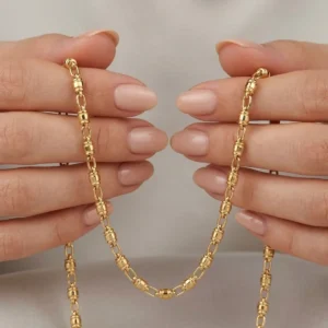 Cadena dorada de eslabones cilíndricos sostenida por manos femeninas en fotografía macro de joyería premium.