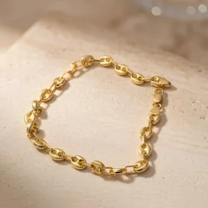 Pulsera Gucci en tono oro con eslabones ovalados y relieves sobre base de piedra beige en fotografía de joyería premium.