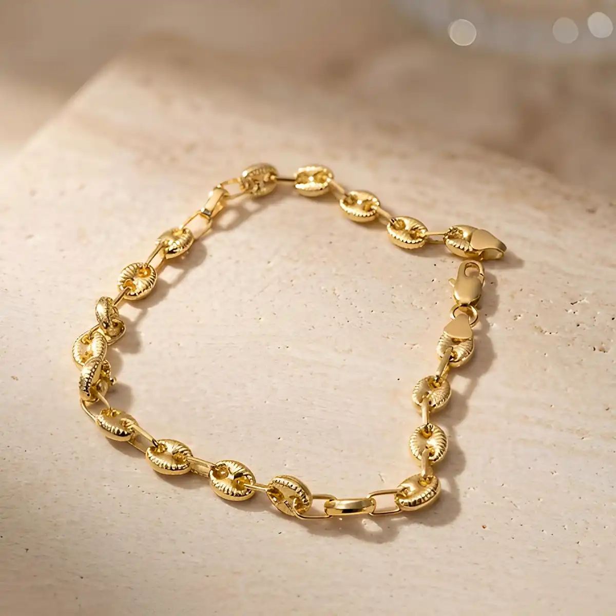 Pulsera Gucci en tono oro con eslabones ovalados y relieves sobre base de piedra beige en fotografía de joyería premium.