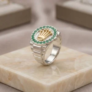 Anillo masculino plateado con corona dorada y circones verdes sobre base de mármol, joya premium de Luxor SM Joyería en Santa Marta.