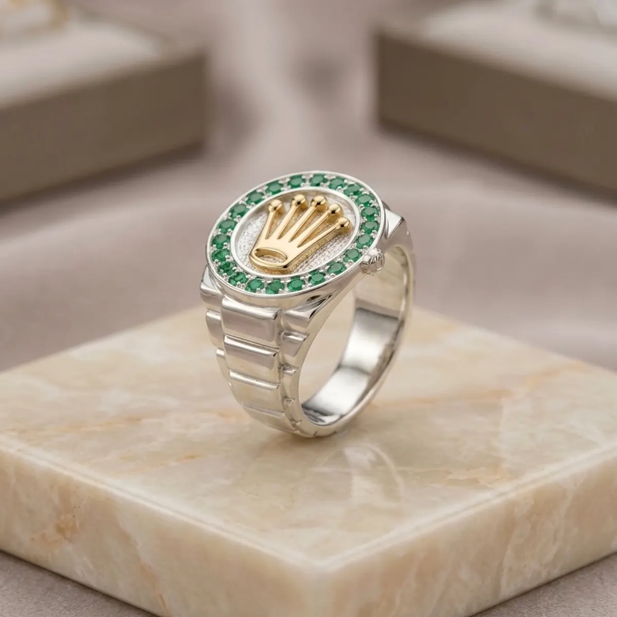 Anillo masculino plateado con corona dorada y circones verdes sobre base de mármol, joya premium de Luxor SM Joyería en Santa Marta.