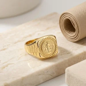 Anillo de San Benito dorado para hombre sobre base de mármol claro, joya religiosa de Luxor SM Joyería en Santa Marta.