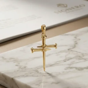 Dije cruz de clavos dorado sobre base de mármol claro, joya religiosa elegante de Luxor SM Joyería en Santa Marta.