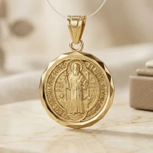 Dije de San Benito dorado con borde facetado sobre base de mármol claro, joya religiosa de Luxor SM Joyería en Santa Marta.