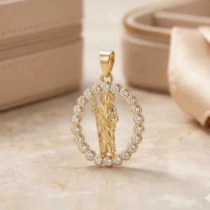 Dije de San Judas dorado con aro de circones sobre base de mármol claro, joya religiosa de Luxor SM Joyería en Santa Marta.