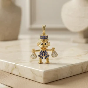 Dije Tío Rico dorado con detalles azules y bolsas de dinero sobre base de mármol claro, joya exclusiva de Luxor SM Joyería en Santa Marta.