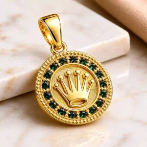 Dije dorado redondo con corona en relieve sobre base de mármol claro, joya elegante de Luxor SM Joyería en Santa Marta.