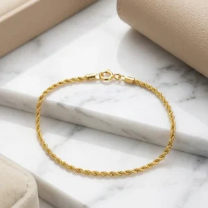 Pulsera lazo dorada de 18 cm sobre base de mármol claro, joya fina de Luxor SM Joyería en Santa Marta.