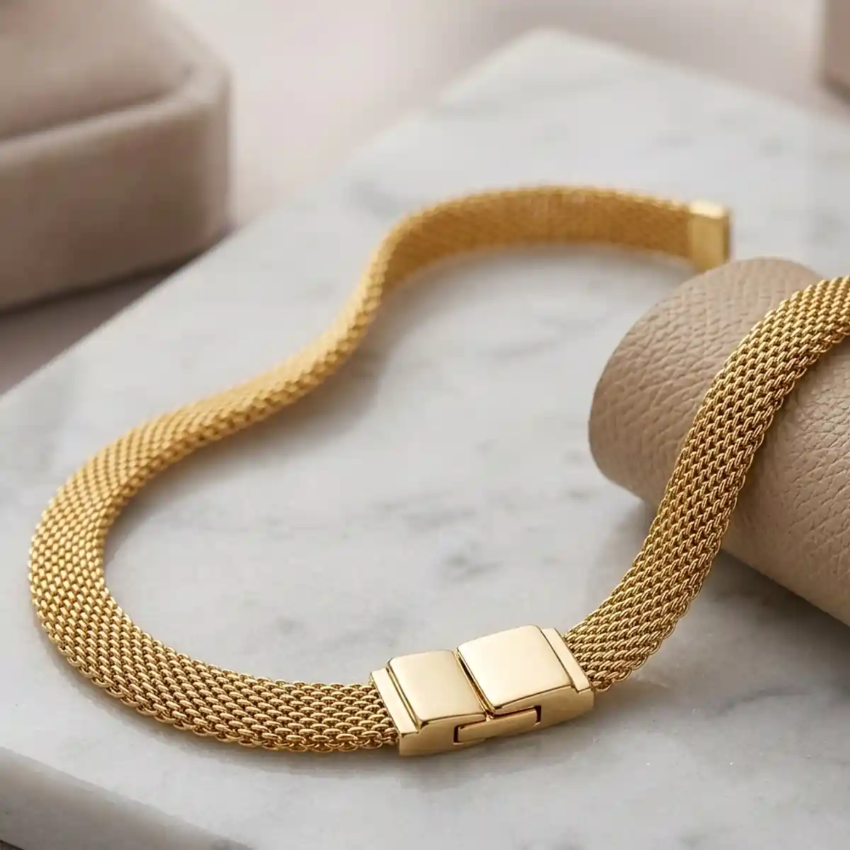 Pulsera tejida dorada tipo malla sobre base de mármol claro, joya elegante de Luxor SM Joyería en Santa Marta.